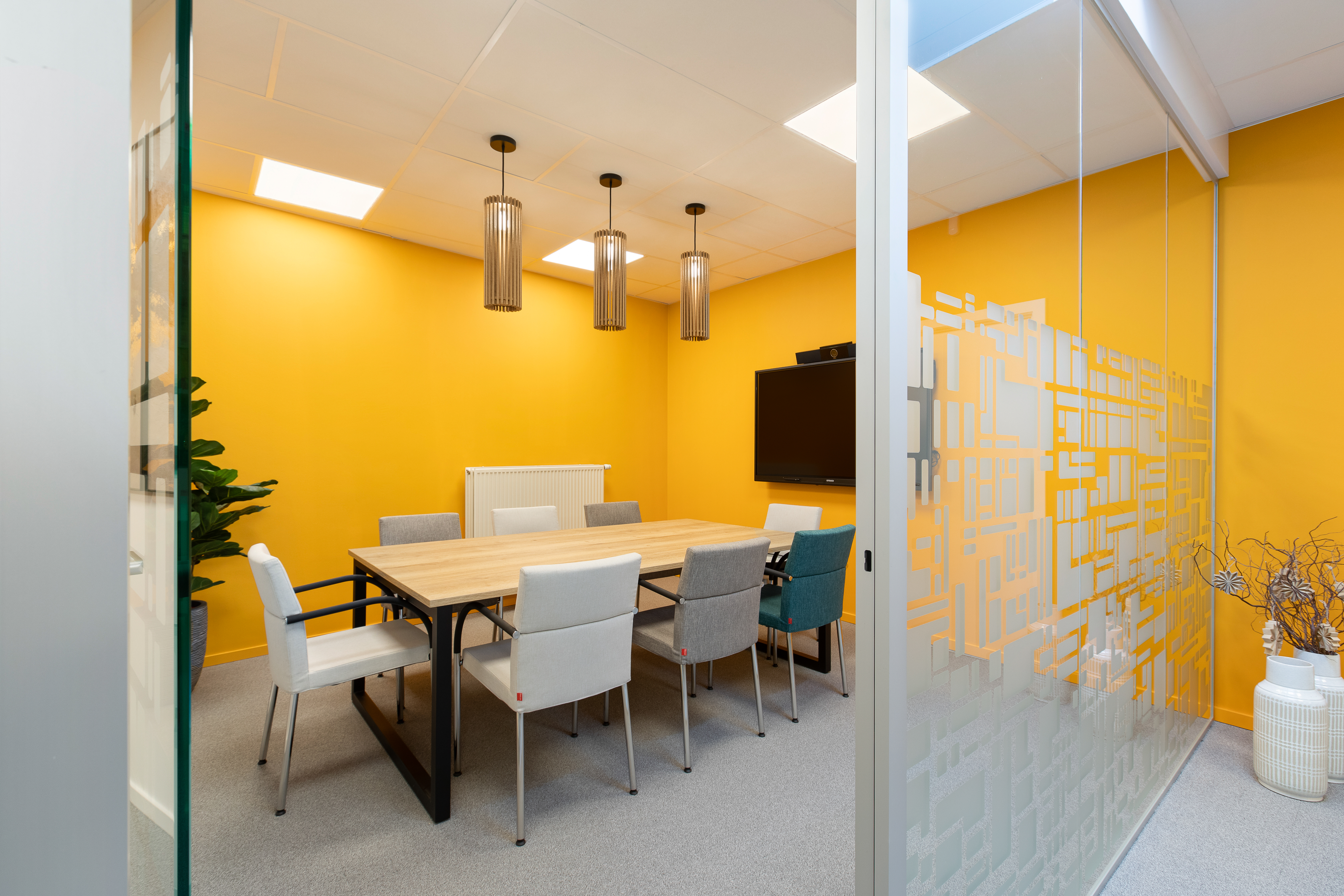 vergaderruimte met gele accentmuur, neutrale vergaderstoelen en vilten sfeerverlichting